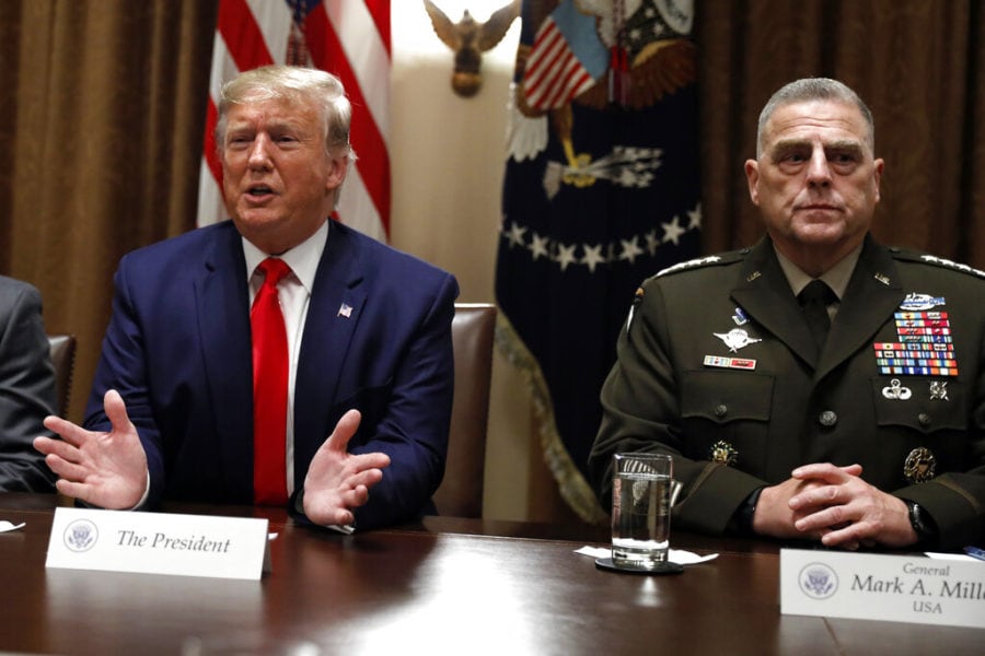 Donald Trump in a navy suit and red tie sits at a conference table, beside General Mark A. Milley in full military dress with ribbons; flags and an emblem backdrop add formal detail.