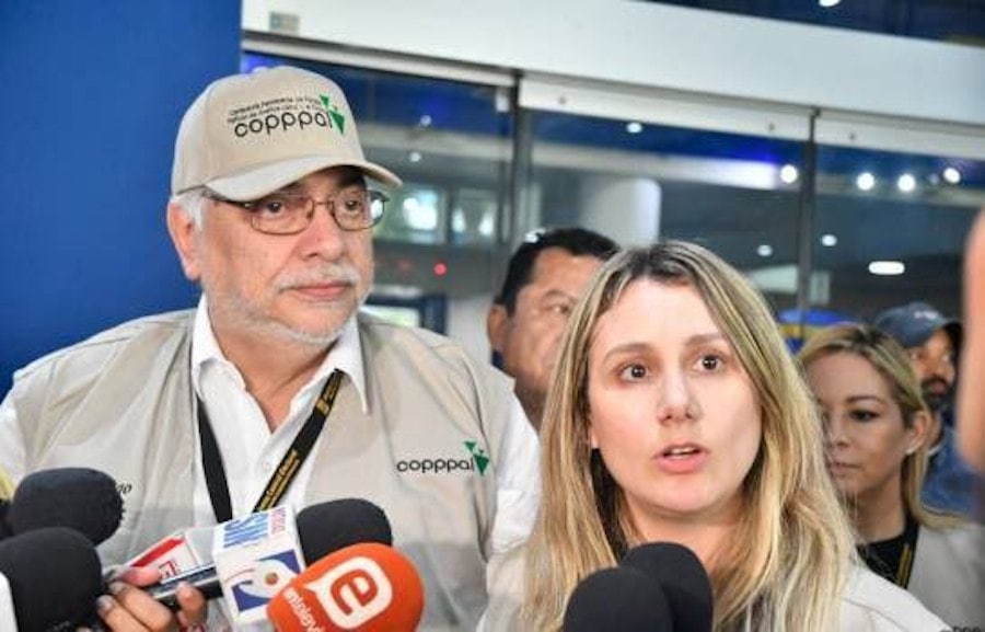 Coppal representatives Ligia Deca, Vicente de la O Levy, and Jual Oram speak to reporters; beige jackets with Coppal logo, microphones in front, busy media backdrop.