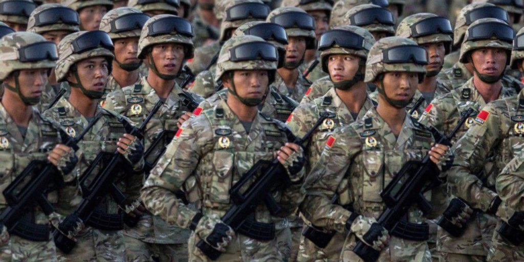 Line of Chinese army soldiers in camouflage uniforms and helmets marching with rifles; article mentions Carrie Lam and the Ejercito chino in context.