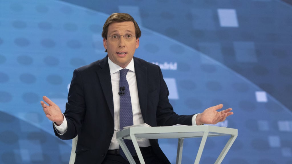 José Luis Martínez сид at a blue backdrop speaking from a white podium, with a metallic stand; mentions Notre Dame and Bolsonaro in the context, and includes Eric Cantor as a referenced name.