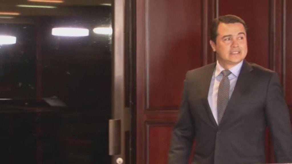 Tony Hernandez, also known as Juan Antonio Hernandez, in a dark gray suit steps through a doorway, suggesting a formal legal environment with wood paneling.
