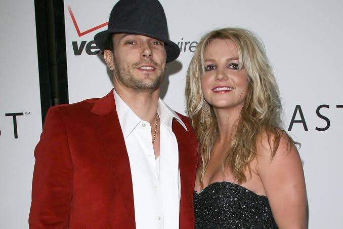 Britney Spears posa junto a Kevin Federline en un evento, con ella en vestido negro brillante y él con chaqueta roja y sombrero negro.