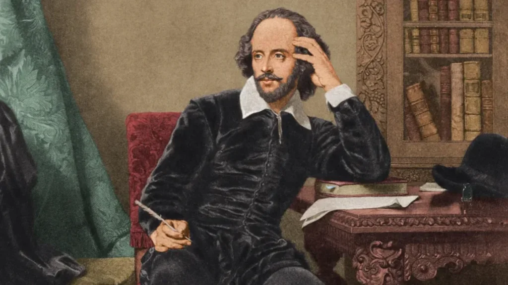 Illustration of William Shakespeare seated, holding a quill, with his hand to his head in thought. He is wearing a dark doublet and white collar, with books and a hat on a desk beside him.